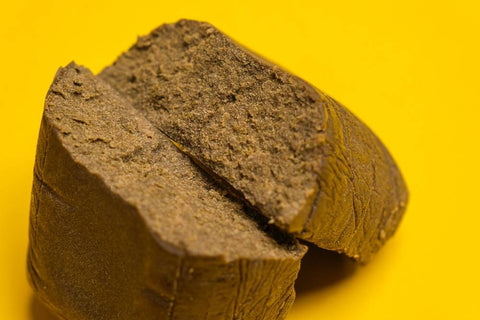 A brick of Critical Purple Kush hash weed is split in half against a yellow background