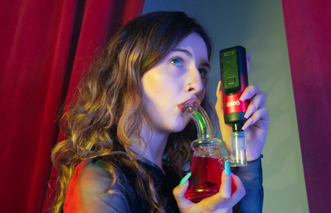 A girl is taking a puff from a red Ooze Glyco freeze bong that has an Ooze Verge dry herb vape inserted