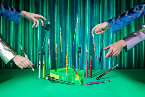 An Ooze Twist Slim Pen Magic Show - Two sets of hands are making all 18 colors of the Ooze TSP 2.0 float in the air in front of a shiny teal curtain.