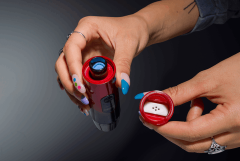 A girl is holding a red and black Ooze Booster with the mouthpiece in her other hand to reveal the blue dish in the Onyx Atomizer.