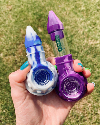 Two Ooze Bowser pipes, the blue white mix and the purple, are held in a hand outside.