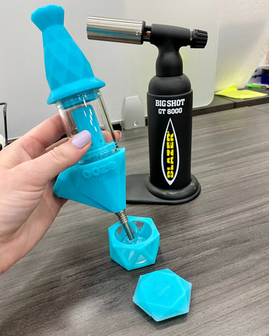 The aqua teal Ooze Bectar is shown being used as a dab straw with a black torch in the background.