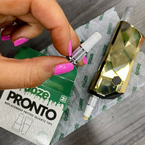 A gold Pronto is laying on a table and a replacement quartz tip is held above it