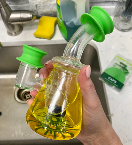A yellow Glyco freeze bong has green Ooze Resolution silicone res caps covering the holes for cleaning