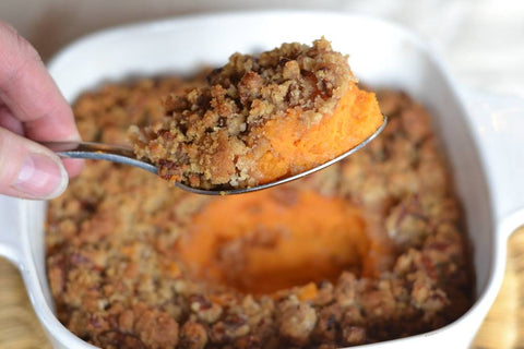 A spoonful of sweet potato casserole with a pecan crust is lifted out of a full casserole dish