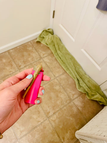 green towel under the door of a bathroom with joint in hand and pink lighter