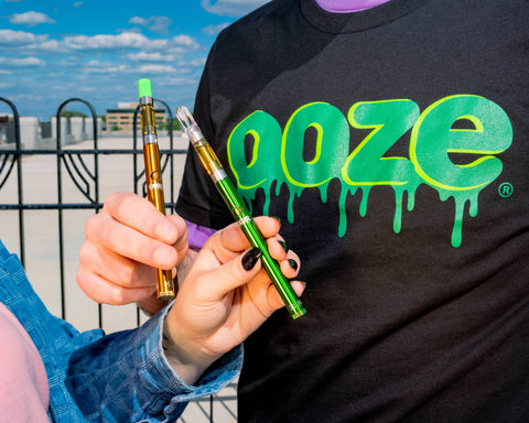 A close-up shot of two people holding Ooze Twist Slim Pens with OozeX cartridges attached.
