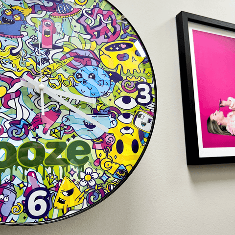 The Ooze Chroma wall clock is hanging on a wall next to a pink photo