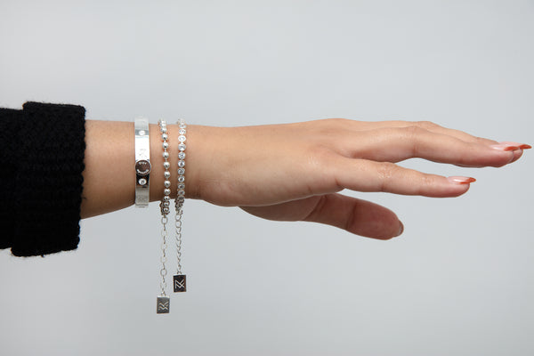 Model wrist and hand showcasing the Miranda Frye Jewelry: silver MF Cuff, silver Fashion Jackson bracelet, and silver Meggan bracelet