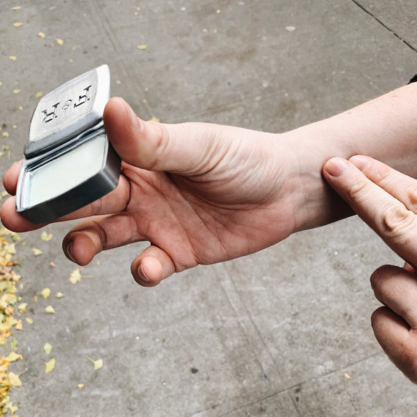 Image of fingers applying solid cologne/fragrance to pulse points (wrist)