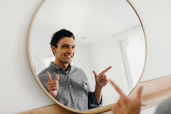 Image of model smiling and doing finger guns in front of the mirror