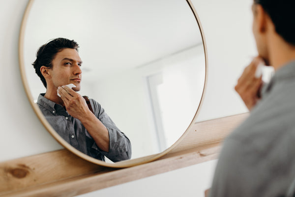 Image of a model looking at a mirror while using aftershave cloths on his face 