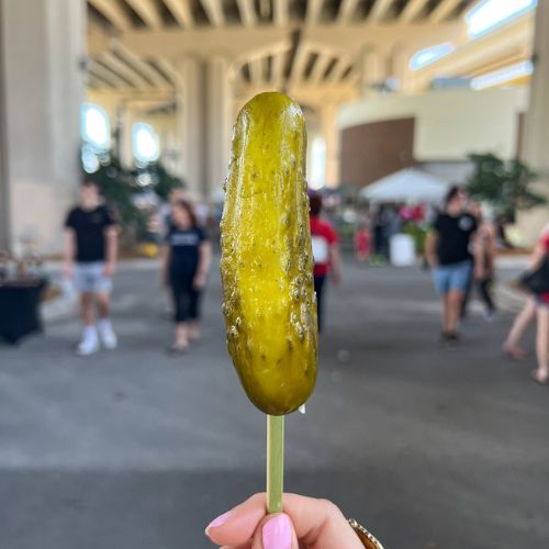 Pickle on a stick with customers and farmers market in distance