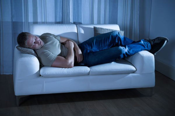 Man sleeping on couch holding his stomach, Gut Health and Sleep Quality