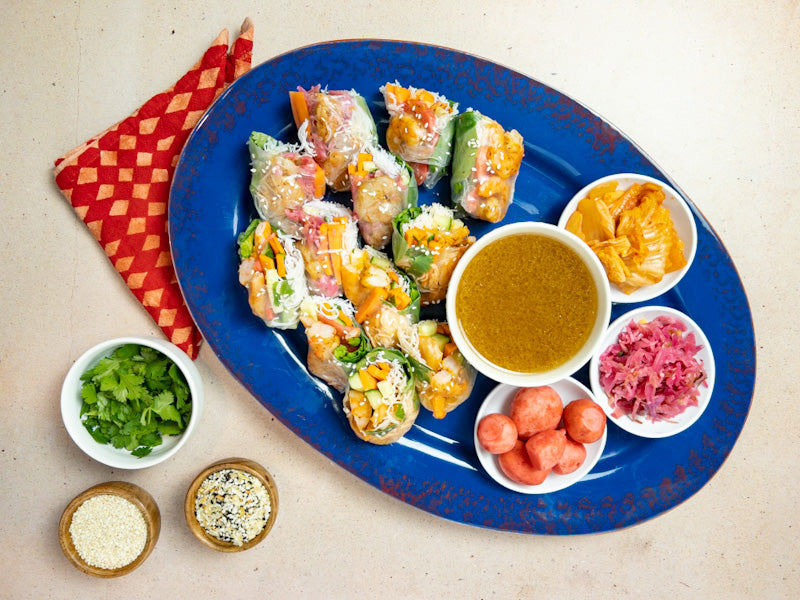 Fresh spring rolls on a platter with bowls of fermented radishes, sauerkraut, and kimchi