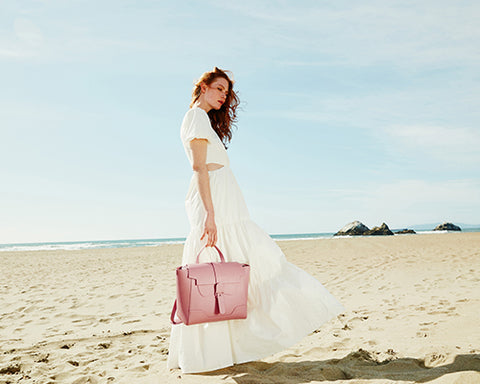 SENREVE model in white maxi dress holding top handle bag