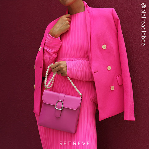 Woman in all pink dress and blazer holding a pink saddle bag with pearl chain