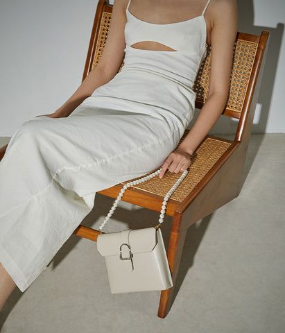 Model in white dress holding white saddle bag
