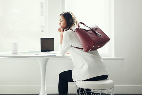 Model working by a desk holding handbag