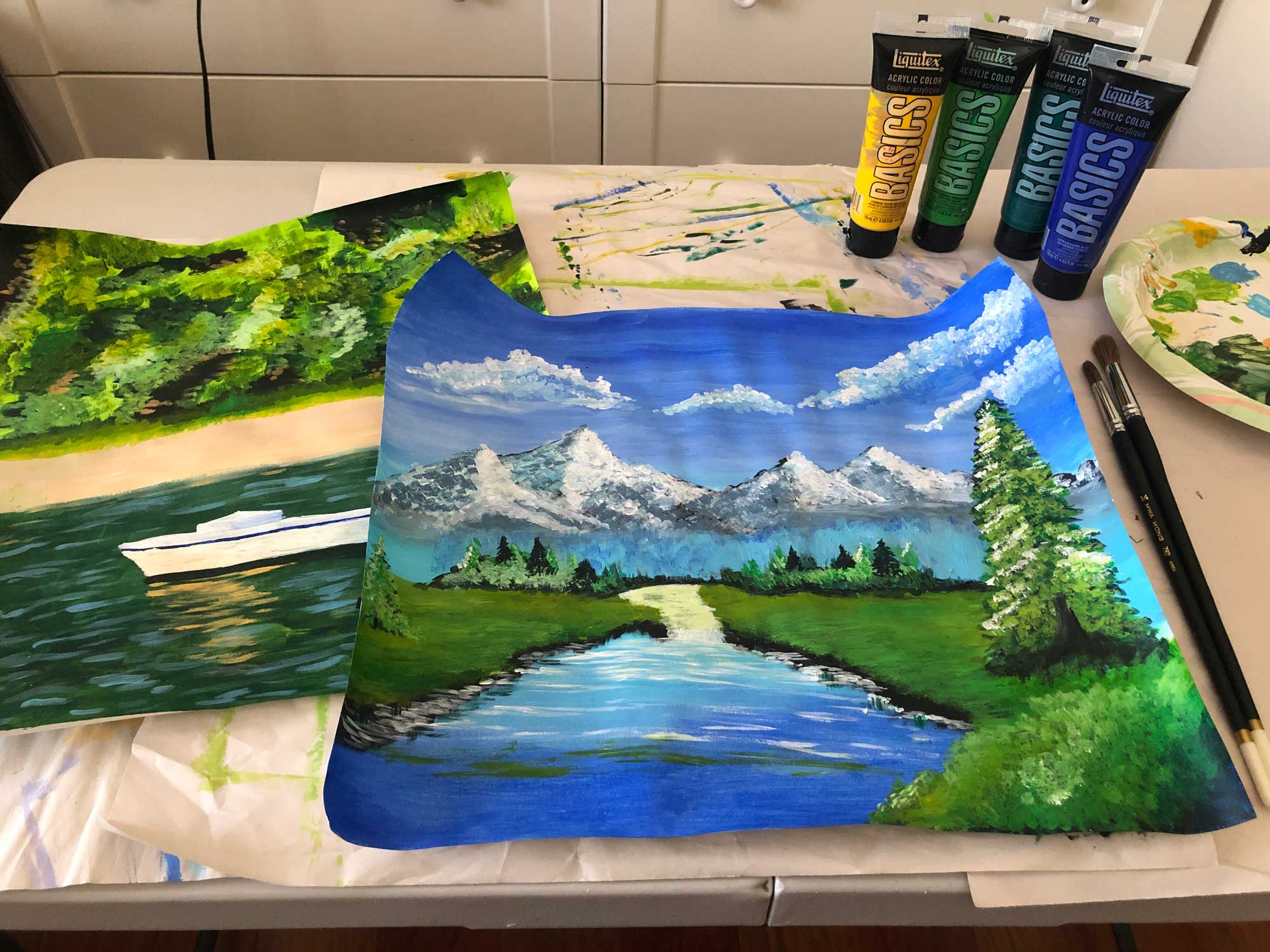Acrylic paints next to painting of landscape