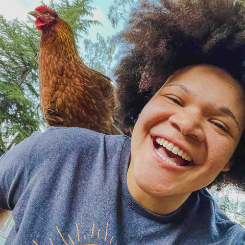 Smiling woman with afro has a chicken sitting on her shoulder.