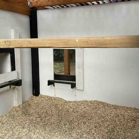 The interior of a chicken coop with a 12 inch deep layer of fine wood chip across the floor. A roosting board is 2 feet above the wood chips.
