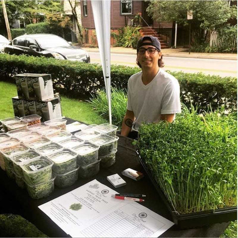 Donny Greens at his farmer's market booth with packages of microgreens for sale and live trays