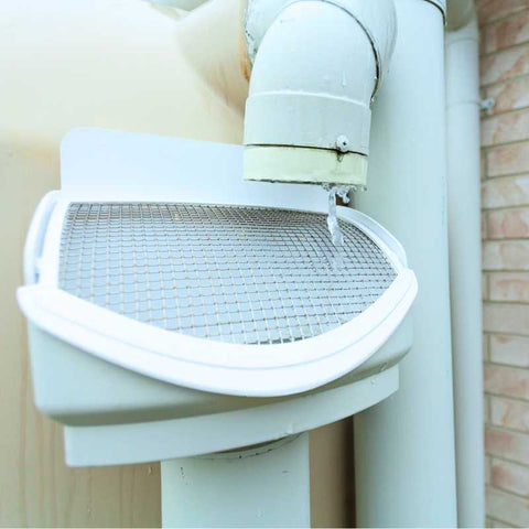 Large white filter covered with a metal grate on a downspout for rainwater harvesting.
