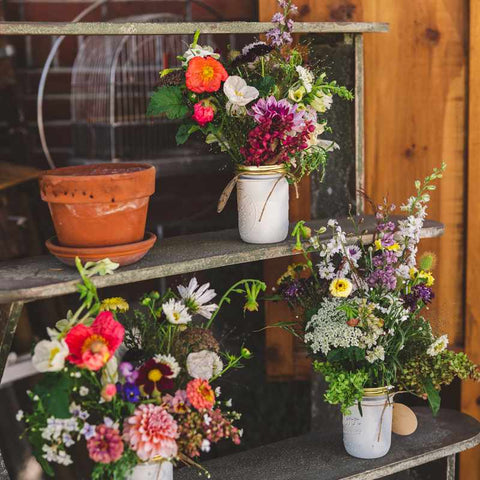 Popup display of floral bouquets in white mason jars on wood shelves.