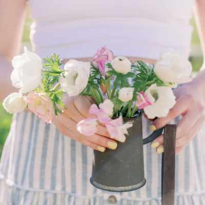 girl holding floral bouquet in white tank top and blue and white skirt with yellow nails