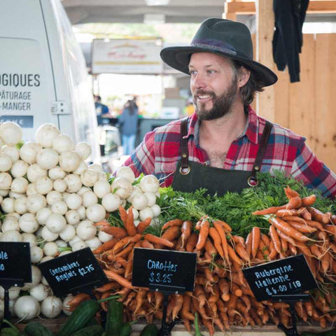 Jean Martin Fortier at Farmers Market Booth standing behind wooden crates filled with vegetables