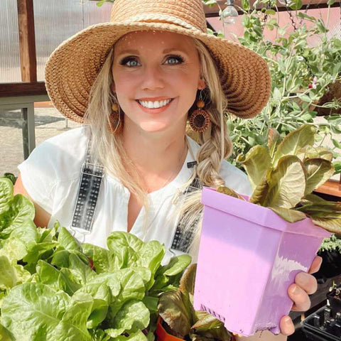 Meg Austin in her greenhouse holding a 5" pot of lettuce