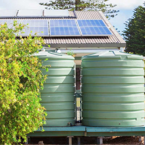 Two large green water collection tanks next to roof with solar panels.