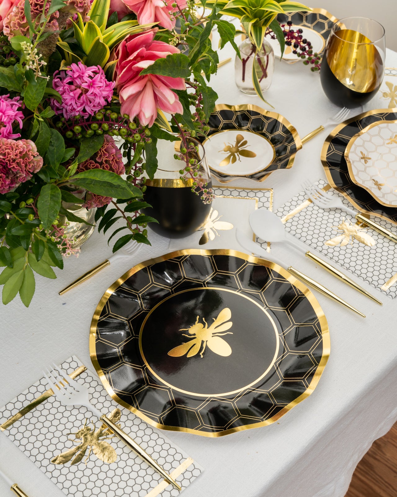 Elegant table setting with floral arrangement, featuring bee-themed black and gold plates and napkins.