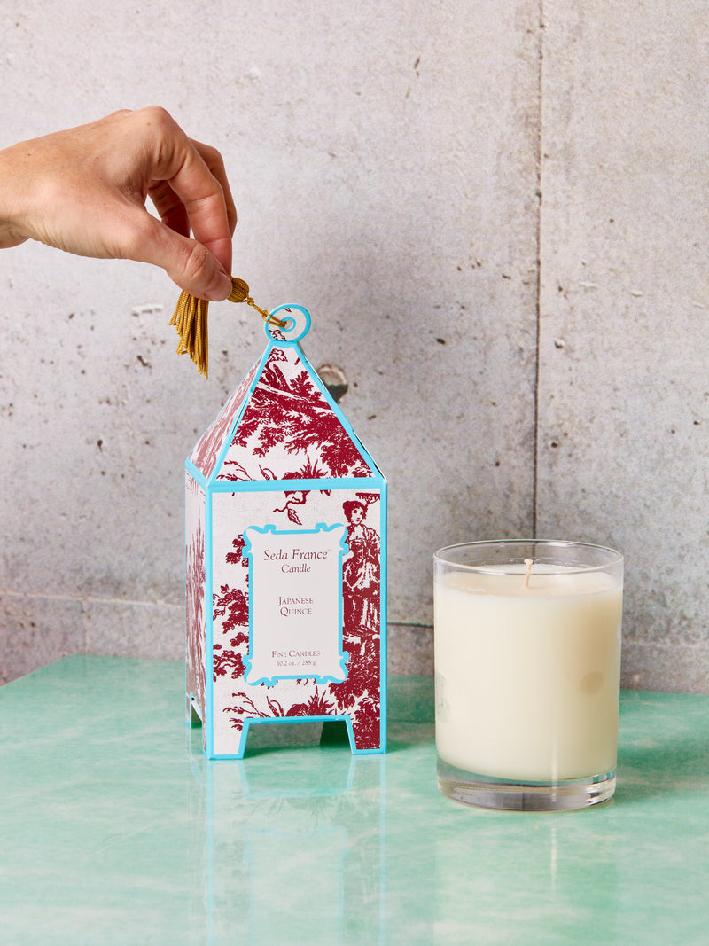 A hand holds the tassel of a Japanese Quince Candles box with a bare candle sitting front right of it.