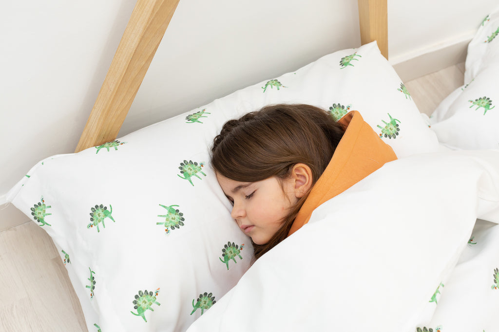 Niña durmiendo en sábanas de dinosaurios verdes