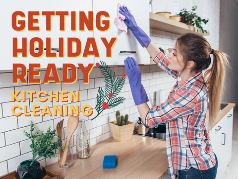 Image features the words "Getting Holiday Ready Kitchen Cleaning" in orange and yellow letters. A caucasian woman with hair pulled back in a ponytail cleans a white kitchen cabinet while wearing rubber cleaning gloves. A blue sponge sits on the wooden counter top with some small decor sitting against white backsplash.