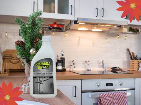 Bottle of Ceramabrye cleaner infront of small fake pine tree in a modern, white kitchen featuring white subway backsplash times, a sparkly range and butcher block counter tops. Small holiday decoratios and a string of lights in the background.