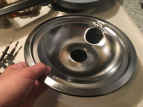 Image of chrome drip bowl held in place by hand on electric range