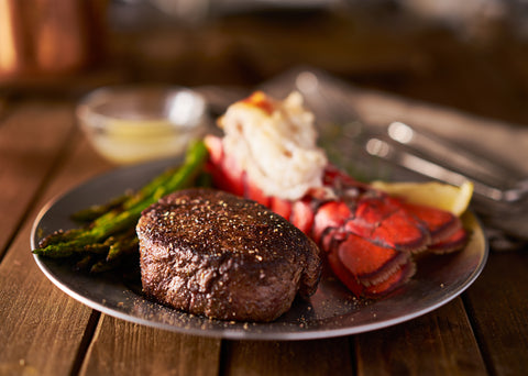 A cooked fillet mignon steak, a cooked open lobster tail and asparagus sit on a plate.