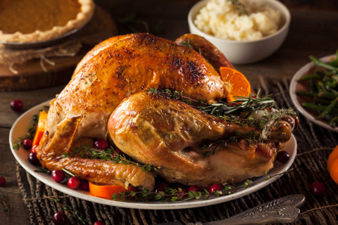 Cooked, golden brown turkey with cranberry accents sits on plate on table. Side dishes sit out of focus in the backgorund.