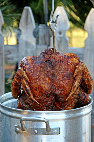 Half of deep fried turkey is pulled out of steel fryer vat in an outdoor setting. 