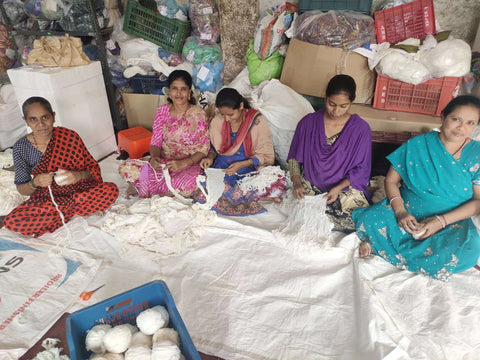 Five of our artisans in India are sitting down on a cloth-covered floor. They are winding white yarn that is soon to be dyed and spun.