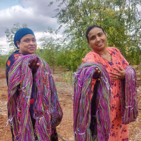 Two Indian artisans are standing outside, holding out unwound skeins of handmade premium silk yarn