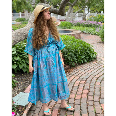 Model is standing in a park wearing a light blue long kaftan.