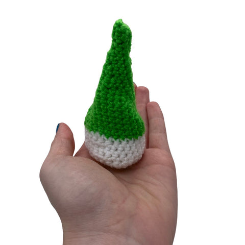 A hand holding out a small elf hat, made out of green and whiteyarn