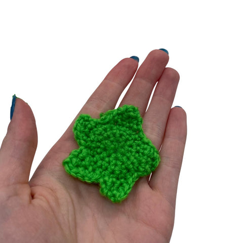 A hand holding out a crochet star made out of green yarn