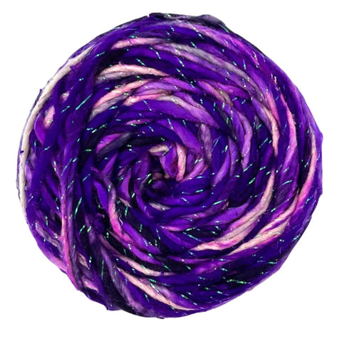 A closeup image of a cake of purple, white, and black sparkle worsted weight silk yarn on a white background.