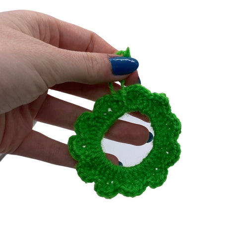 A hand with blue nails dangling a crochet wreath made out of green yarn