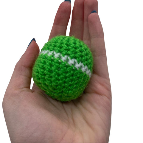 A hand holding out a circular ball ornament, made out of green and white yarn